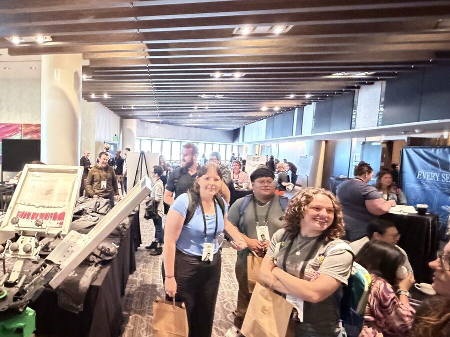 Smiling conference guests holding kraft merch bags beside a live press station